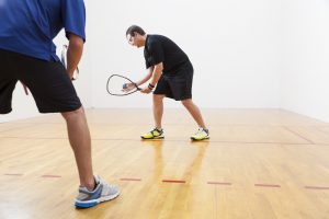 Two men playing racquetball on court. One serving.